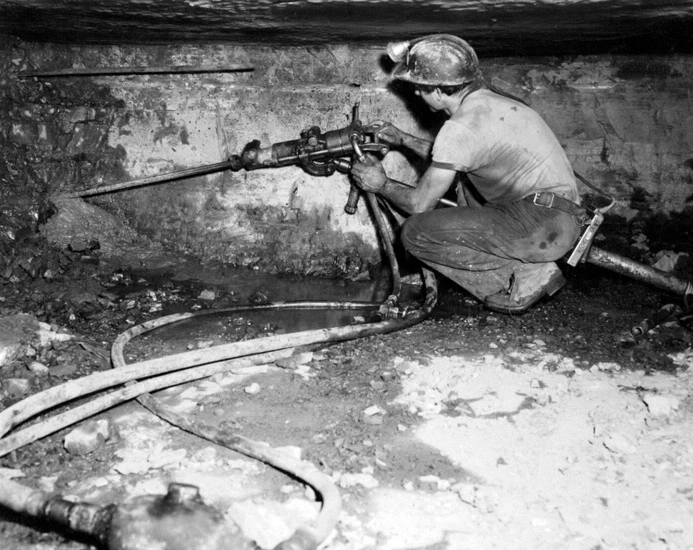 Black and white photo of a miner drilling a shaft