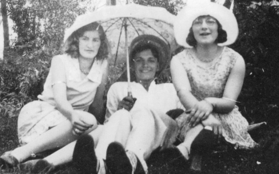 Three women sitting down. One is holding an umbrella.